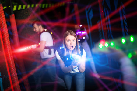 Portrait of girl in colored beams of laser guns during laser tag game on dark arena