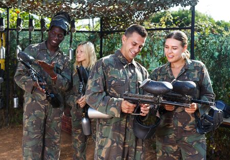 Paintball players in protective form with masks and marker guns preparing for game. Focus on manの写真素材