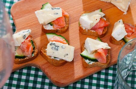 Delicious canapes on toasted bread with smoked salmon, cambozola, cucumber and creamy sauce on wooden boardの写真素材