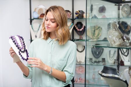 Portrait of happy young woman demonstrating natural amethyst  stone necklace in shopの写真素材