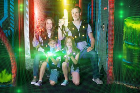Modern young parents and children with laser pistols posing together in bright beams in laser tag labyrinthの写真素材