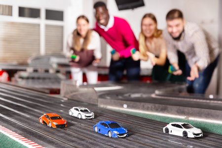 Cheerful happy men and women play together with the slot car racing track
