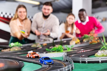 Cheerful and smiling men and women play together with slot car racing trackの写真素材