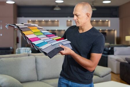 Portrait of positive smiling man showing various samples of textures for furniture in shopの写真素材