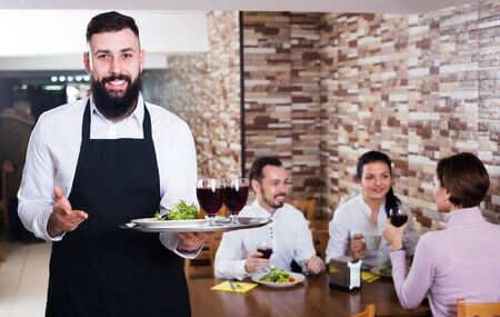 Nice male waiter showing country restaurant to visitorsの写真素材