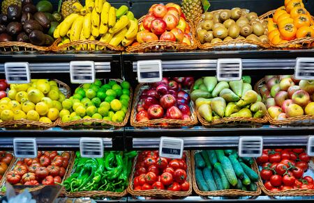 Large assortment of fresh colorful fruits and vegetables in wicker trays on shelves in supermarketの写真素材