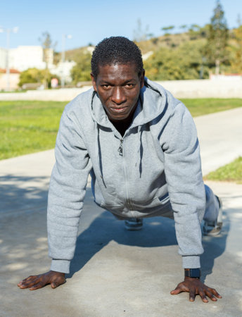 Athletic young male in sportswear training different exercises at park outdoor
