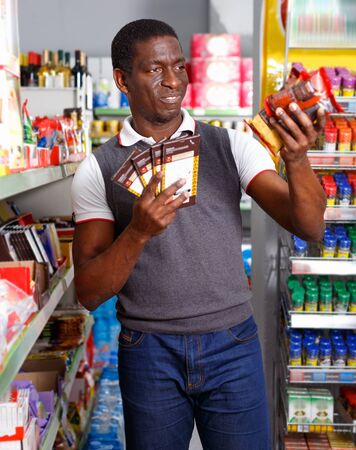 Portrait of  cheerful positive  Afro man buying chocolate sweets in storeの写真素材