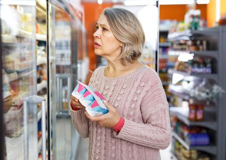 Portrait of senior woman choosing fresh dairy products on shelves in grocery shopの写真素材