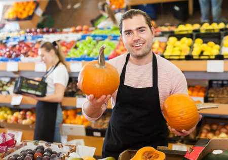 Fine man with pumpkin in hands wearing apron on the supermarketの写真素材