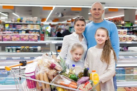 Ordinary kids with parents are standing with purchases in the supermarketの写真素材