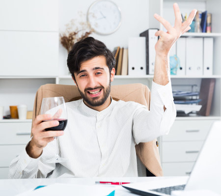 Relaxed brunette businessman drinking red of wine in officeの写真素材