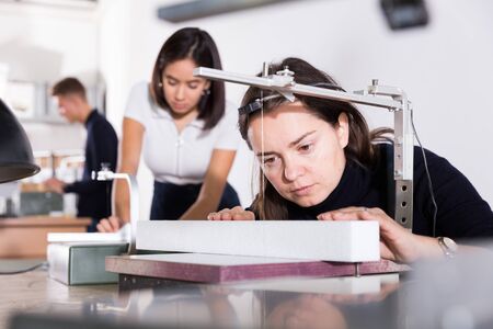 Focused woman working in architecture modeling workshop, using scroll saw for cutting styrofoam elementsの写真素材