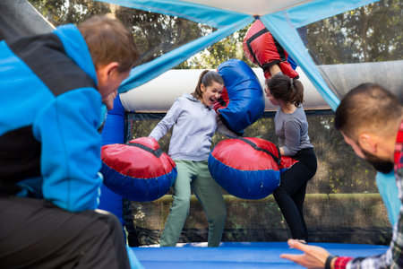 Happy female friends fighting by big stuffed boxing gloves at outdoor amusement playground