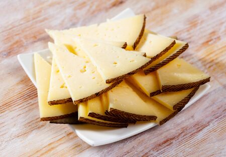 Appetizing slice of semi-hard cheese on wooden surfaceの写真素材