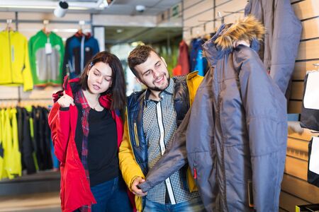 Glad couple examining windcheaters in sports clothes shop. Focus on manの写真素材