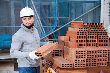 Serious young man working on his house renovations, stacking red bricksの写真素材