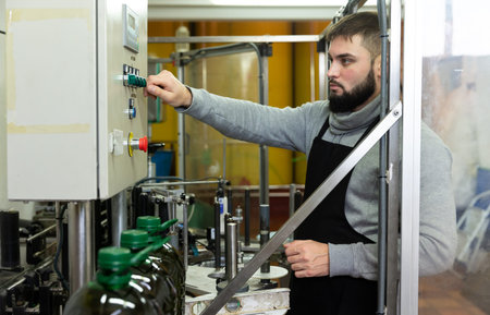 Portrait of skilled guy working on conveyor for bottling olive oil in plastic bottles in small...