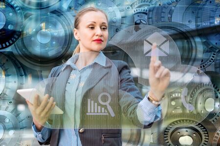 Businesswoman with tablet in hand standing on mechanical device background, pressing email icon on virtual digital touchscreenの写真素材