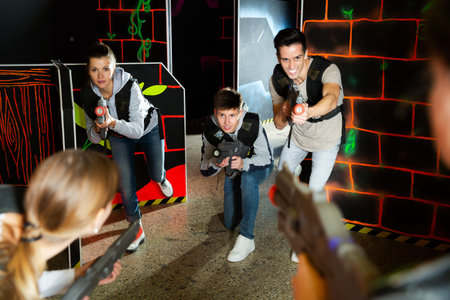 Group of adult friends with laser pistols having fun in dark room