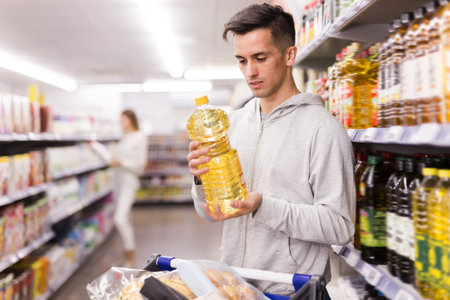 Portrait of man with shopping cart choosing olive oil in store