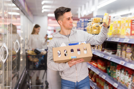 Ordinary male customer with cardboard box buying food products in supermarket