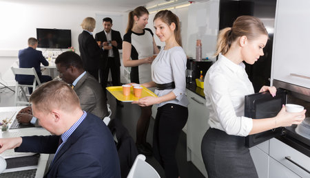 business men and women rest in a break in the office talking and drinking hot drinks