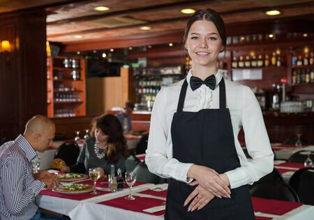 Portrait of polite waitress wearing black apron in restaurant interiorの写真素材
