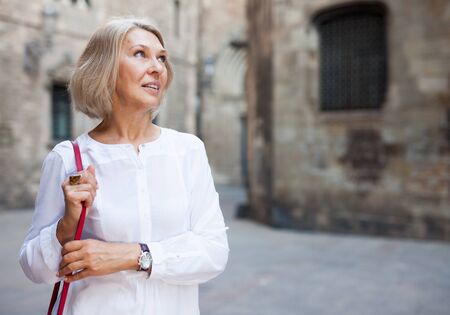 Cheerful mature female is walking in white blouse on the street outdoorの写真素材