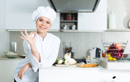 Smiling female kitchener in uniform is standing in the kitchen at the restaurant.の写真素材