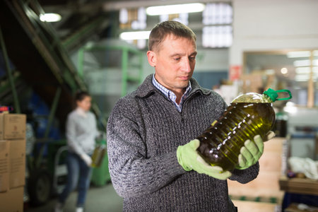 Successful owner of small olive oil factory working at warehouse, checking plastic bottles filled of...