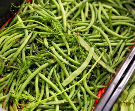 Closeup of fresh pods of green beans in plastic punnets on market counterの写真素材