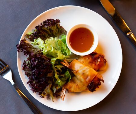 Traditional Thai dish - fried spring rolls with shrimp served with piquant sauce and fresh greensの写真素材