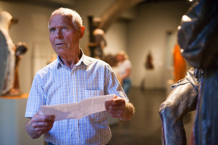 Positive elderly man with guidebook standing at hall of Art Museum