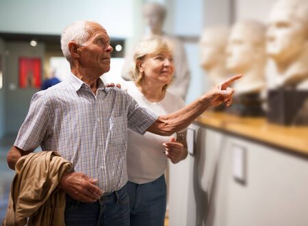 Positive elderly couple looking at exhibits on exposition of museumの写真素材