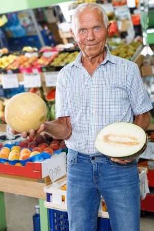 Positive elderly male customer searching for fresh fruits in greengroceryの写真素材
