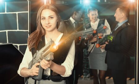 Lucky woman and her colleagues on background having corporative entertainment in laser tag roomの写真素材