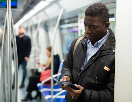 Focused African man absorbed in his smartphone while traveling in subway carの写真素材