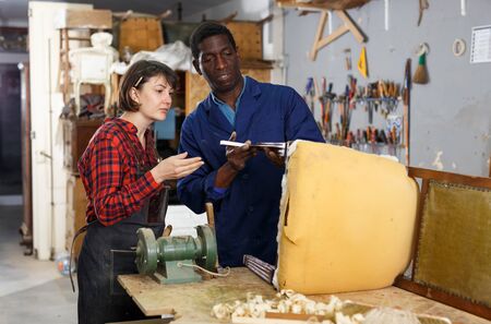 Portrait of male and female artisans inspecting vintage armchair in workshopの写真素材