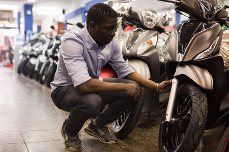 Afro american man is shopping and choosing new motobike in moto store