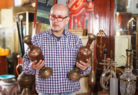 serious  adult man visiting shop of antique goods in search of interesting objects