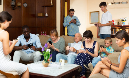Portrait of modern multiracial family absorbedly looking at mobile phones at home