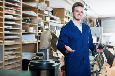 Young smiling guy joiner working with professional drill at workshop