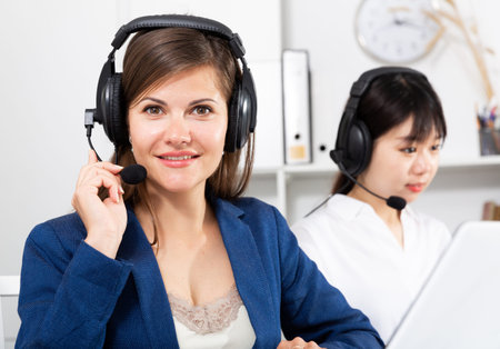 Friendly smiling woman helpline operator with headset using computer at office
