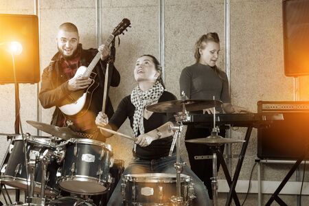Music garage band with expressive cheerful girl drummer rehearsing in sound studioの写真素材