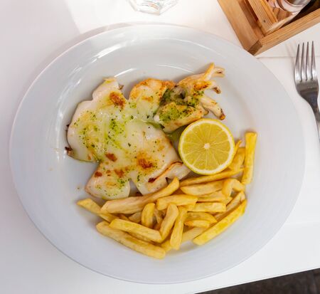 Appetizing fried sepia flavoured with savory green sauce served on white plate with fries and lemonの写真素材