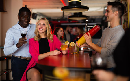 Bartender shaking cocktail for friends, they drinking in nightclub