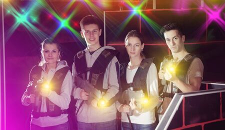 Four happy young men an women posing with laser pistols in their hands in dark laser tag roomの写真素材