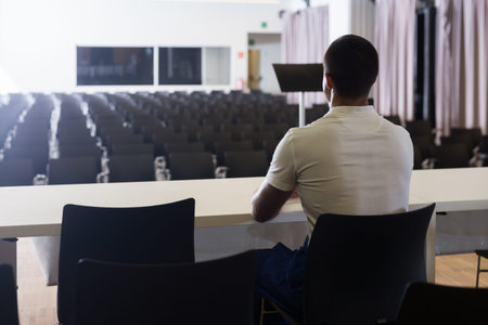 Man sitting at the table on stage opposite to empty conference hall