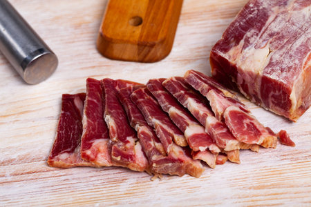 Delicious Capocollo made from dry-cured pork neck with cut pieces on wooden table. Traditional...